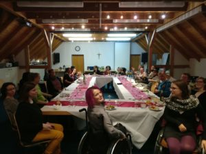 Gruppe sitzt am Tisch und winkt in die Kamera