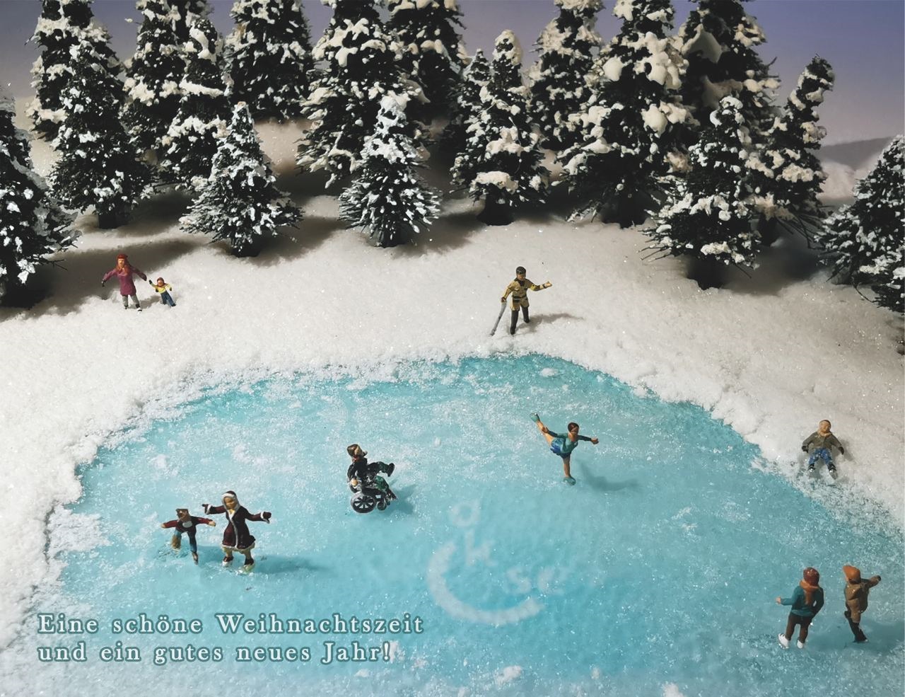 In einer verschneiten Winterlandschaft, die durch einen gefrorenen See, Schnee und Bäume dargestellt wird befinden sich mehrere Personen mit und ohne sichtbare Behinderung. Alle vergnügen sich. Einige fahren zum Beispiel mit Schlittschuhen auf dem gefrorenen See. In der Mitte des Sees ist das Logo von aktiv und selbstbestimmt e.V. zu erahnen. Links unten steht folgendes: „eine schöne Weihnachtszeit und ein gutes neues Jahr!“
