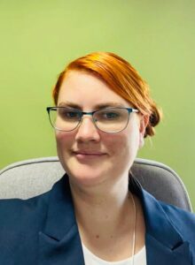 Eine Frau mit roten Haaren und einer Brille vor einem grünen Hintergrund 